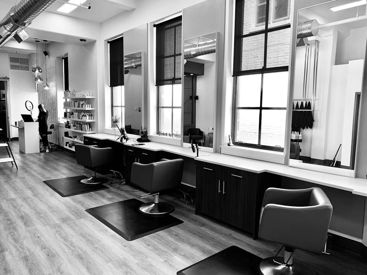 A bright, empty hair salon with styling chairs and large windows